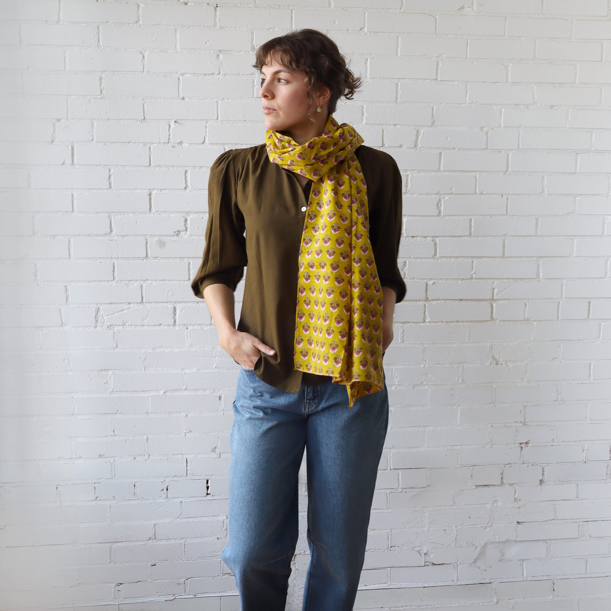 Person wearing a yellow patterned scarf against a white brick wall