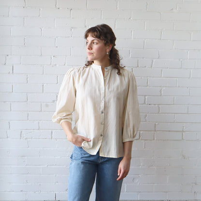 Woman wearing a cream blouse and blue jeans against a white brick wall