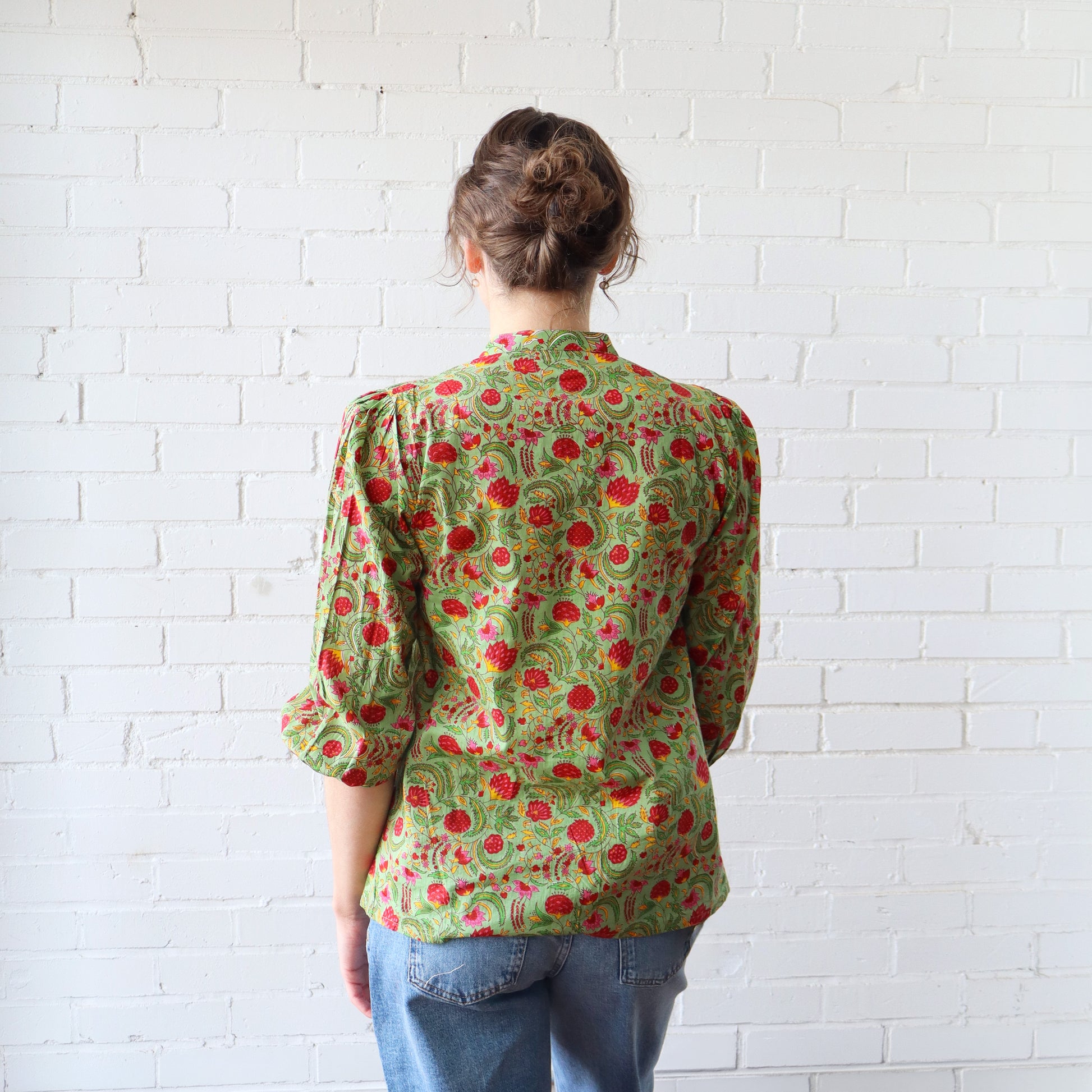 Person wearing a green floral blouse against a white brick wall