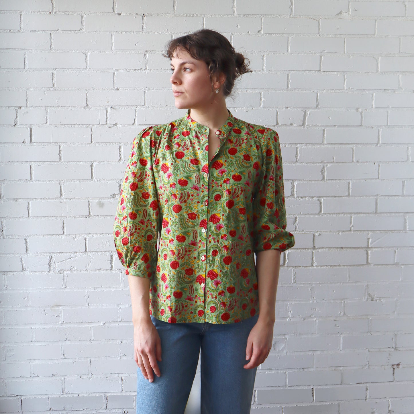 Woman wearing a green floral blouse against a white brick wall