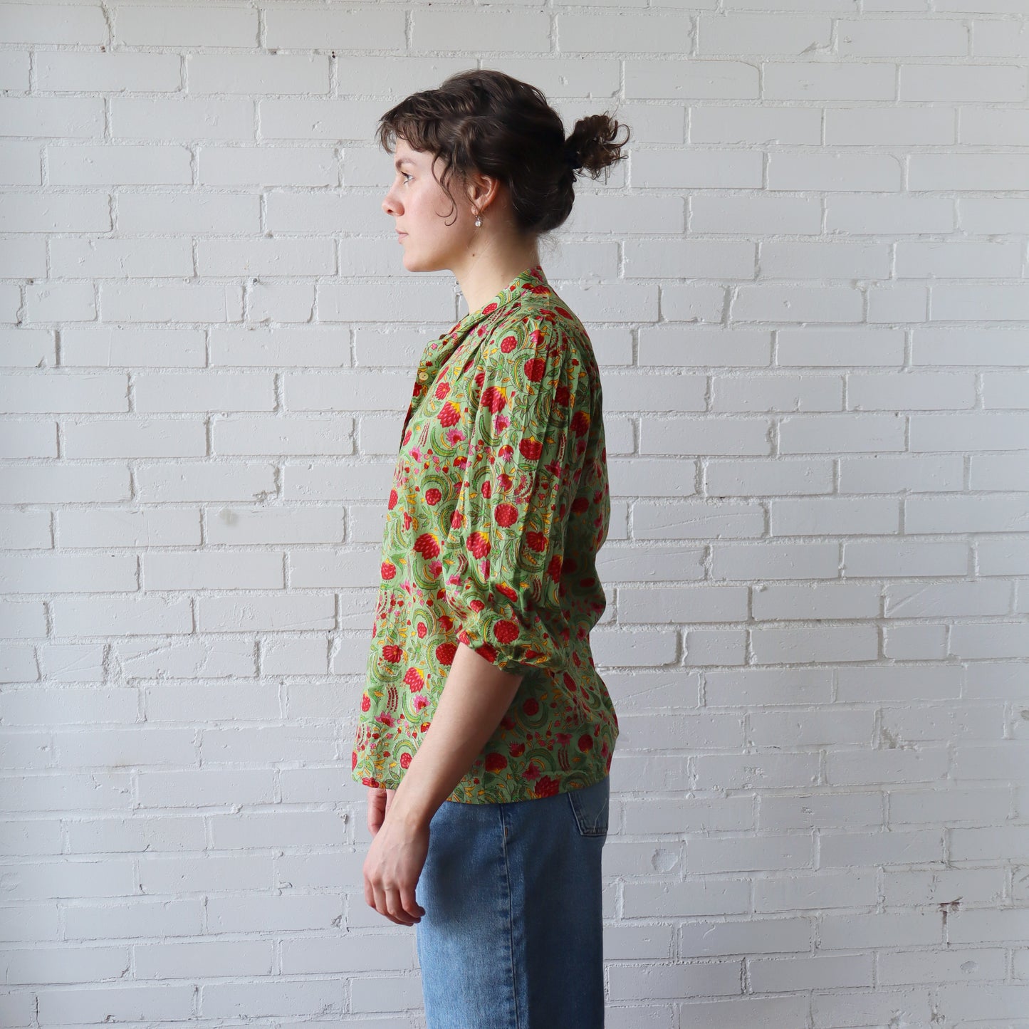 Person wearing a green floral shirt against a white brick wall