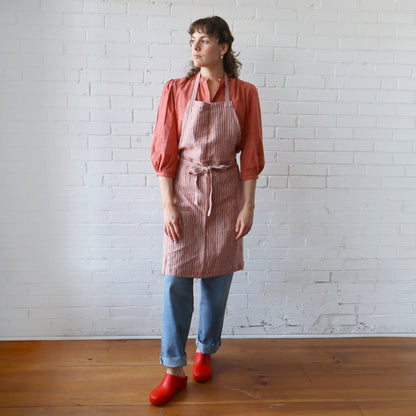 Person wearing a red and white striped apron against a white brick wall.
