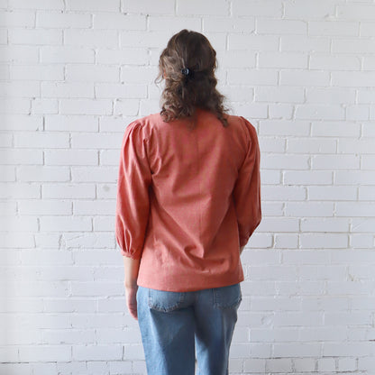 Person wearing a pink blouse and blue jeans standing against a white brick wall.