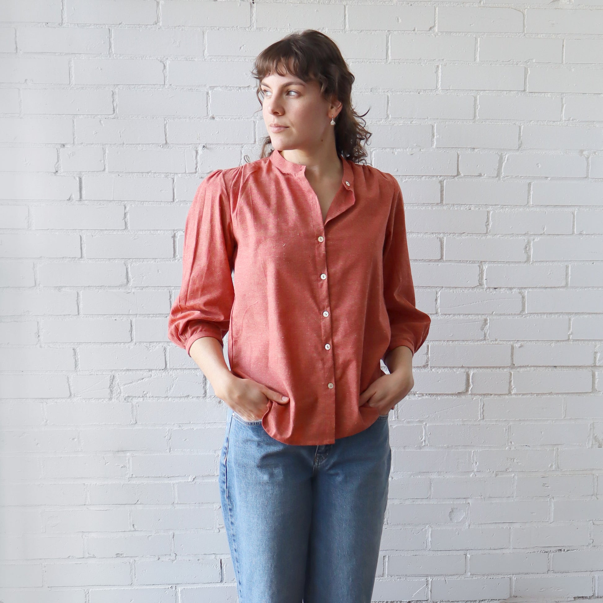 Woman wearing a coral shirt and blue jeans against a white brick wall