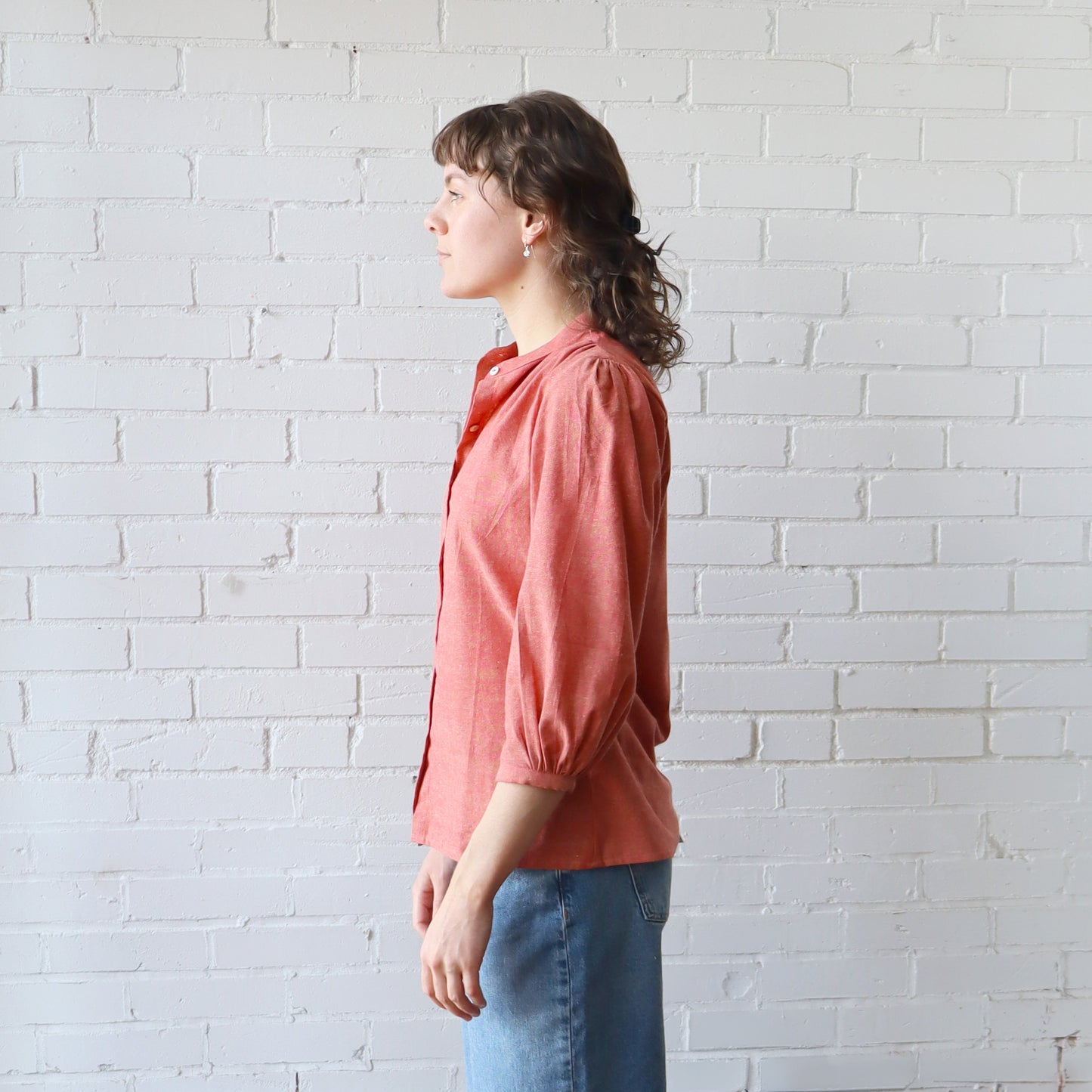 Woman wearing a pink blouse and blue jeans against a white brick wall