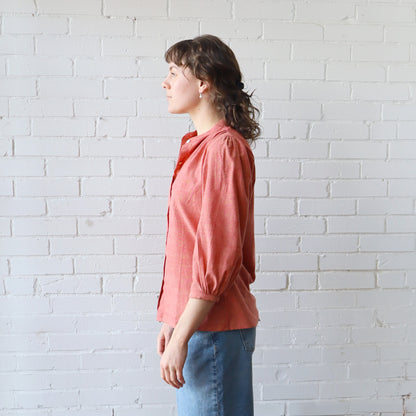 Woman wearing a pink blouse and blue jeans against a white brick wall