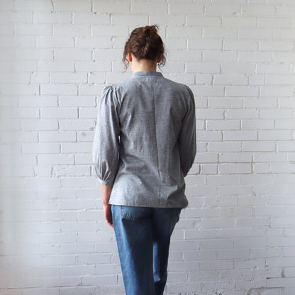 Person wearing a gray shirt and blue jeans standing against a white brick wall.