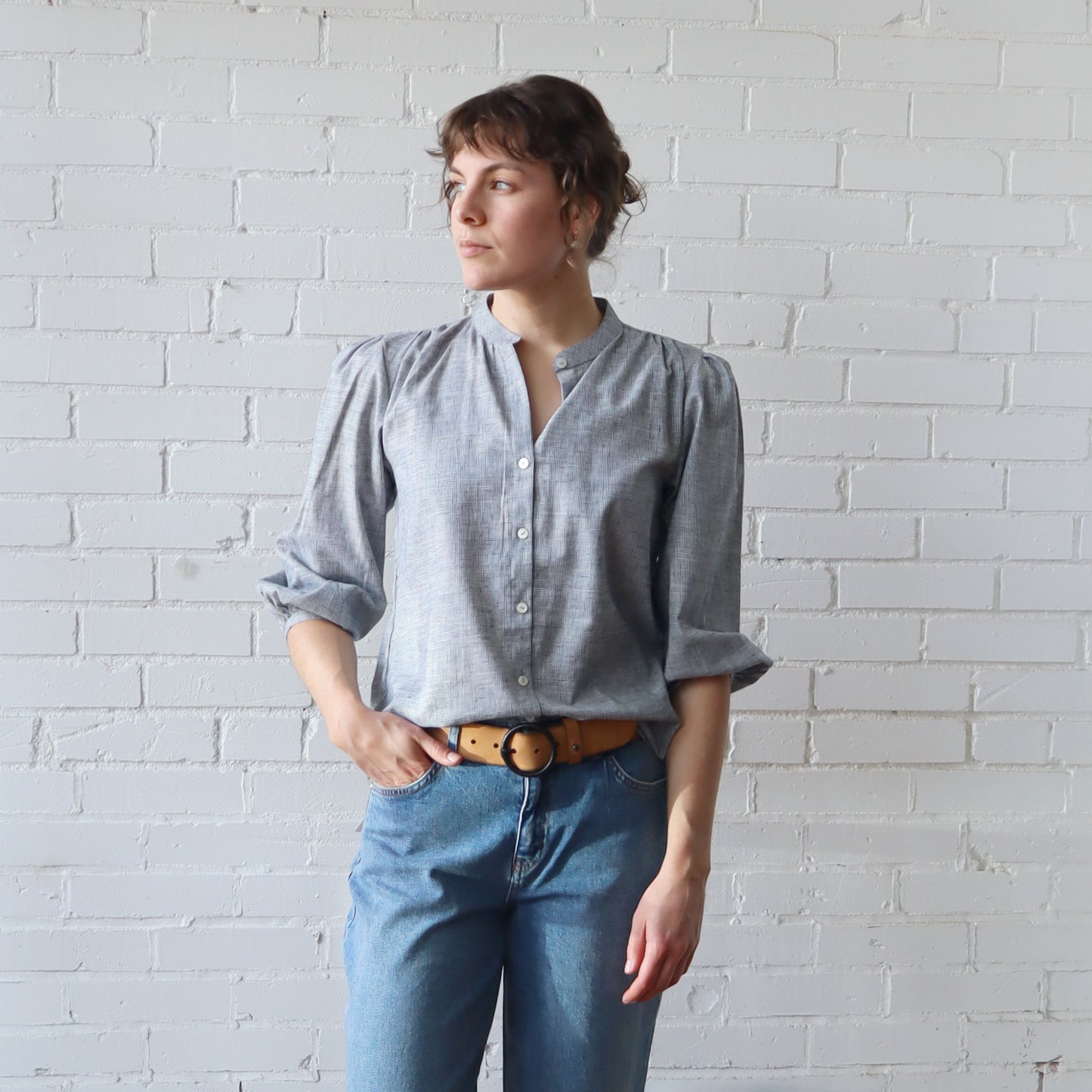 Woman wearing a light blue shirt and jeans against a white brick wall