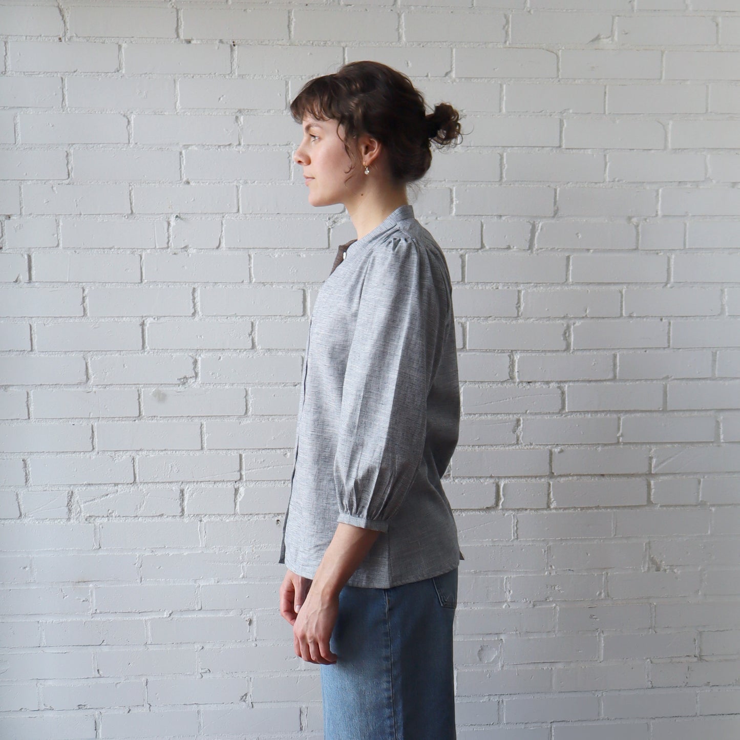 Person wearing a gray shirt and blue jeans standing against a white brick wall.