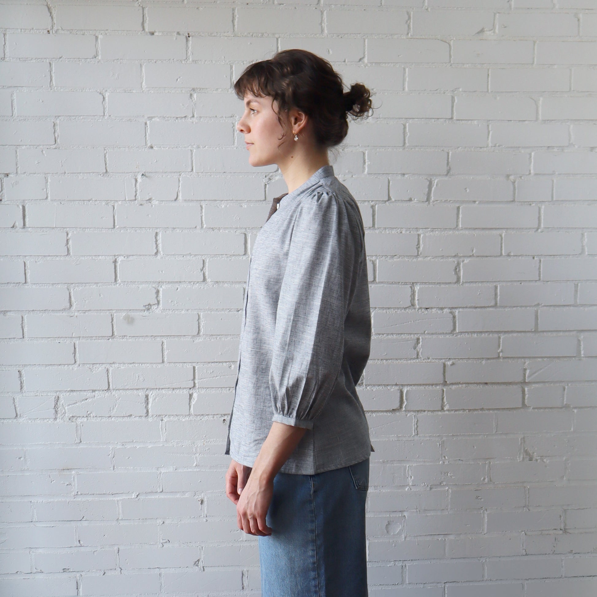 Person wearing a gray shirt and blue jeans standing against a white brick wall.