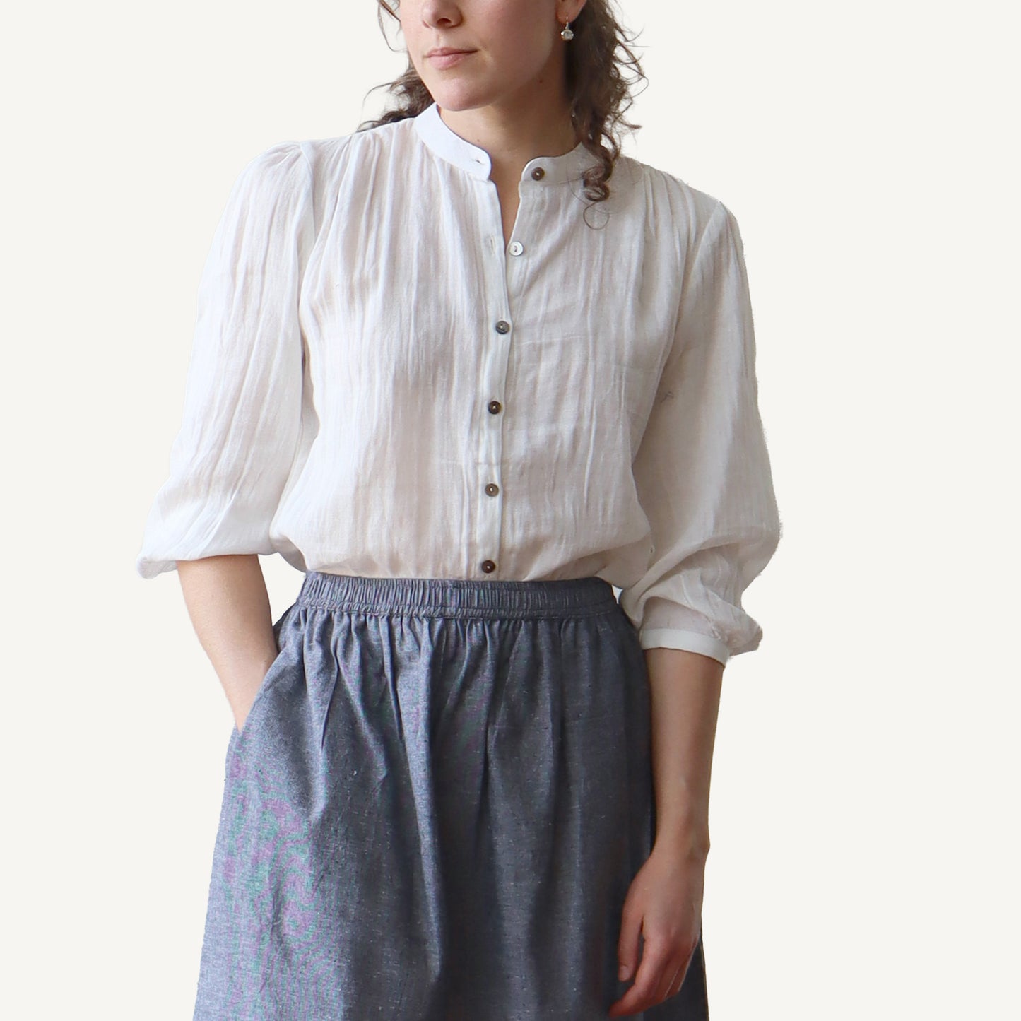 Person wearing a white blouse with puffed sleeves and a gray skirt on a plain background
