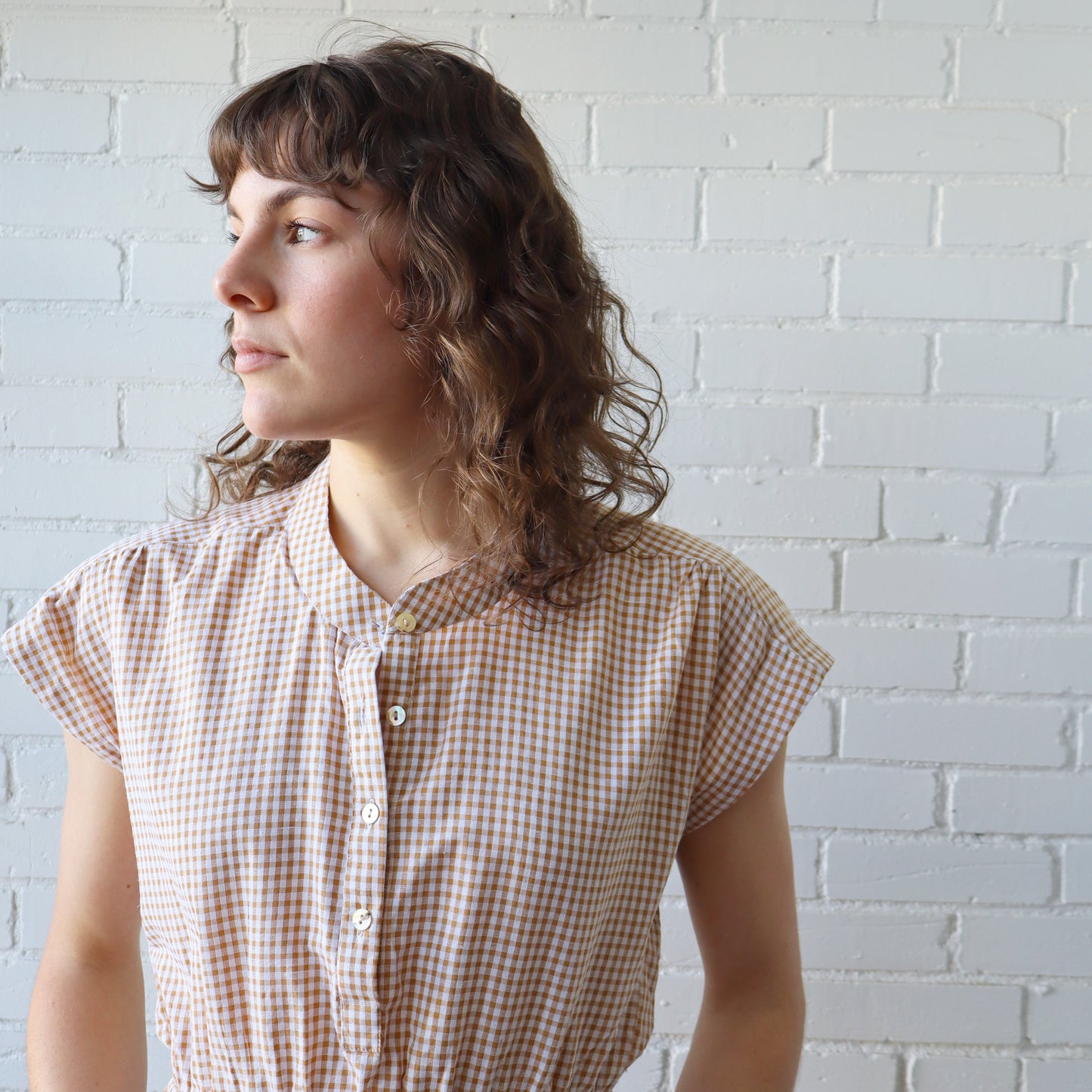 Woman wearing a checkered shirt against a white brick wall