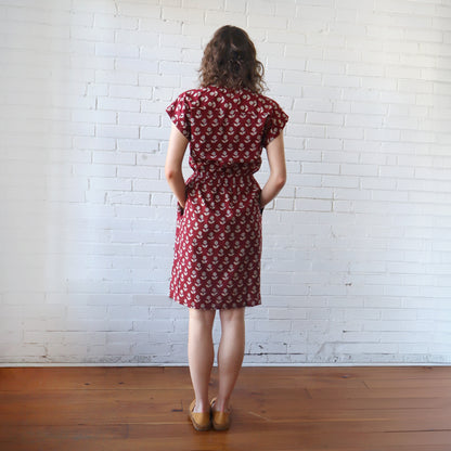 Woman wearing a red patterned dress against a white brick wall.