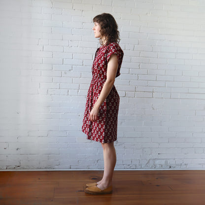 Woman wearing a red patterned dress standing against a white brick wall.