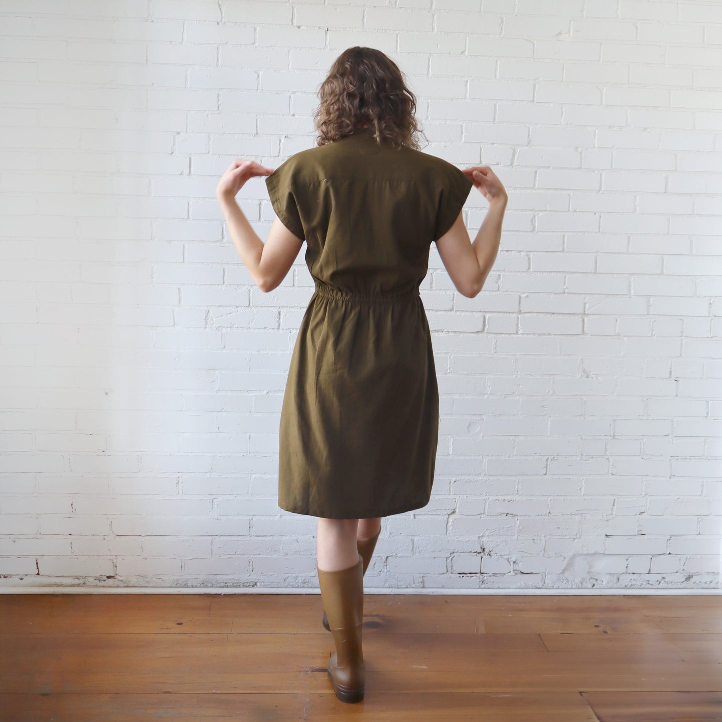 Woman wearing a green dress standing against a white brick wall.