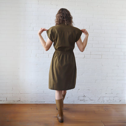 Woman wearing a green dress standing against a white brick wall.
