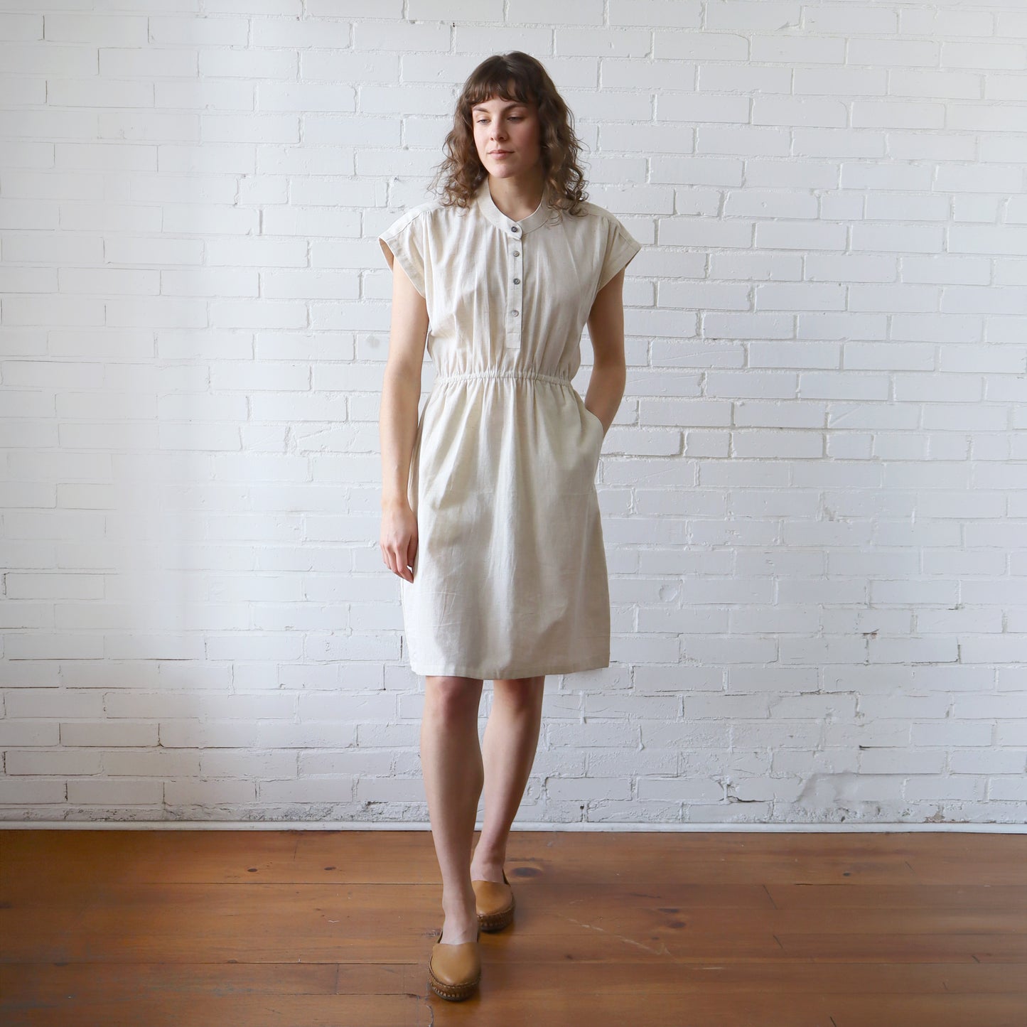 Woman wearing a white dress standing against a white brick wall.