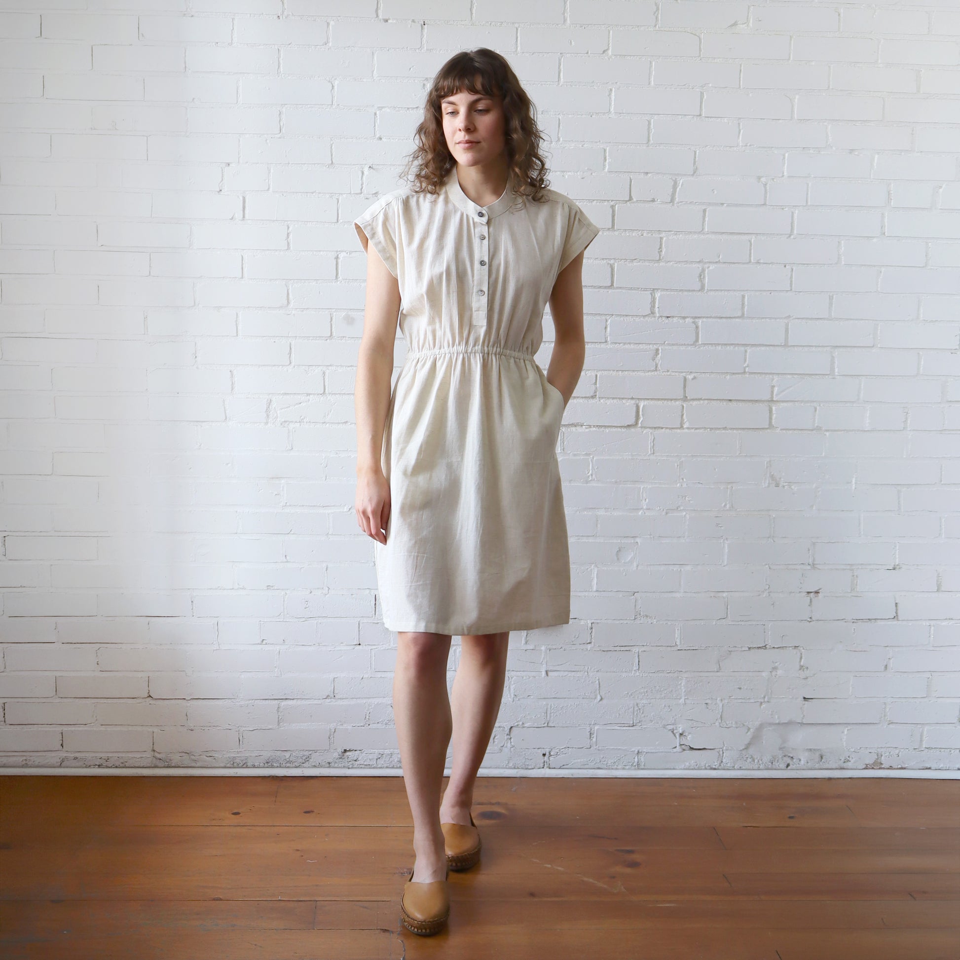 Woman wearing a white dress standing against a white brick wall.