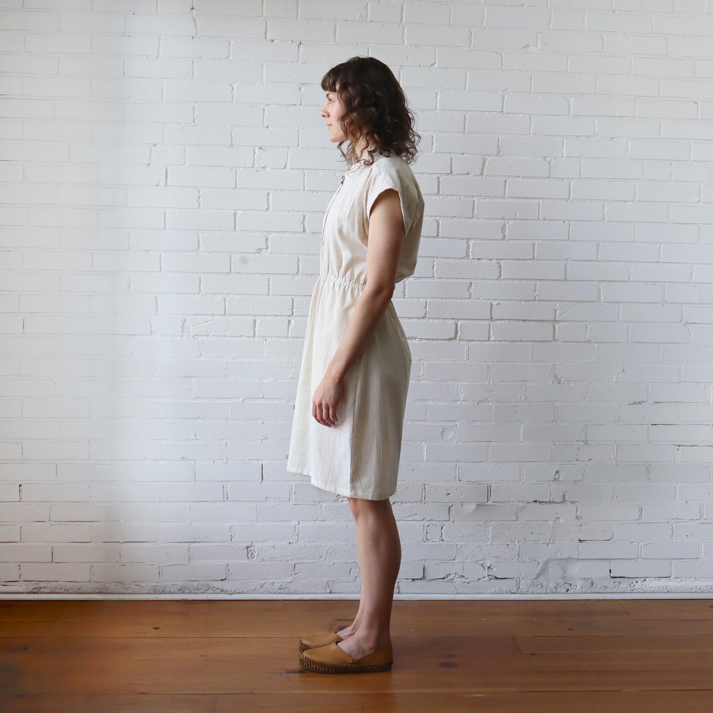 Woman in a white dress standing against a white brick wall.