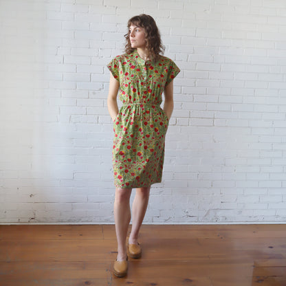 Woman wearing a green floral dress standing against a white brick wall.