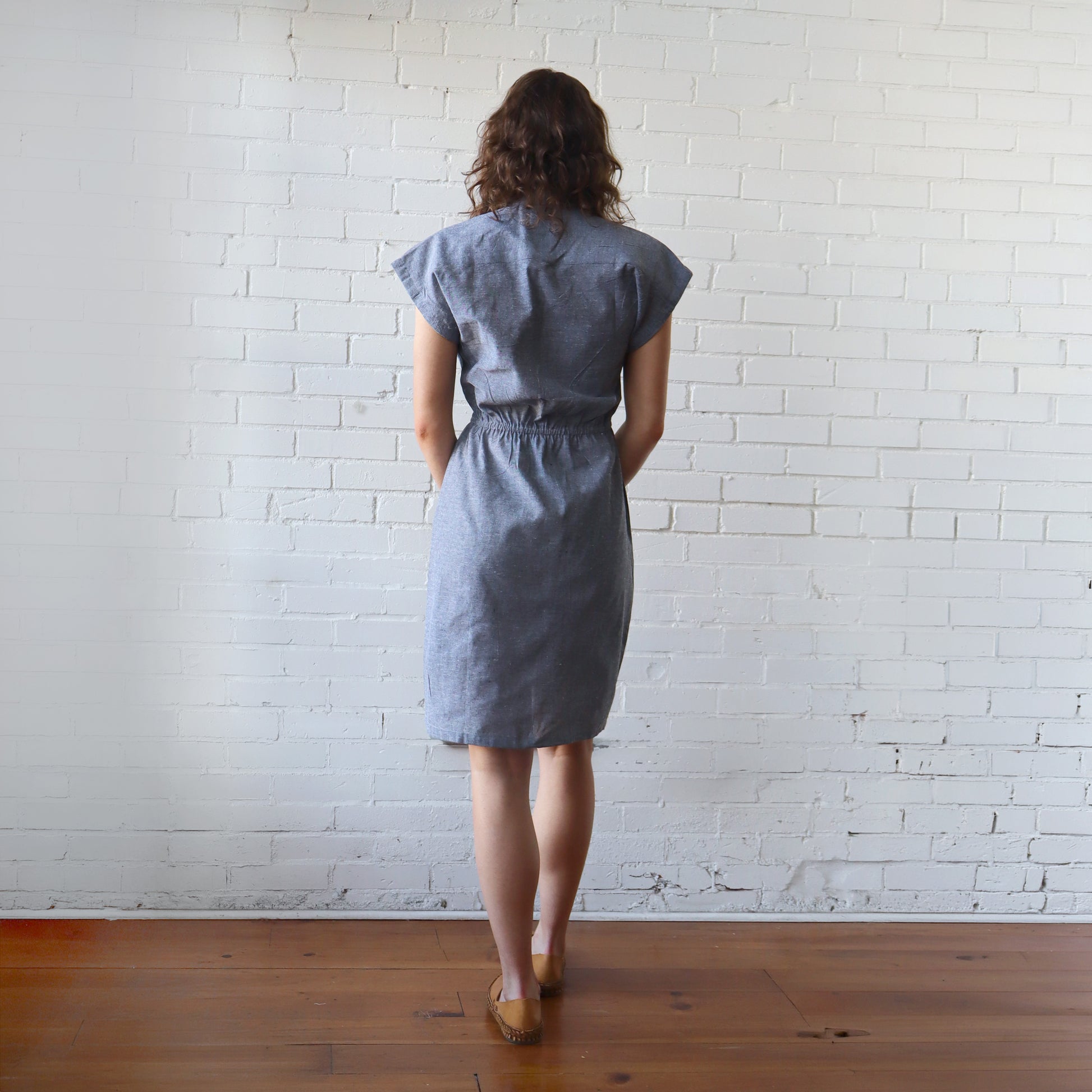 Woman wearing a blue dress standing against a white brick wall.