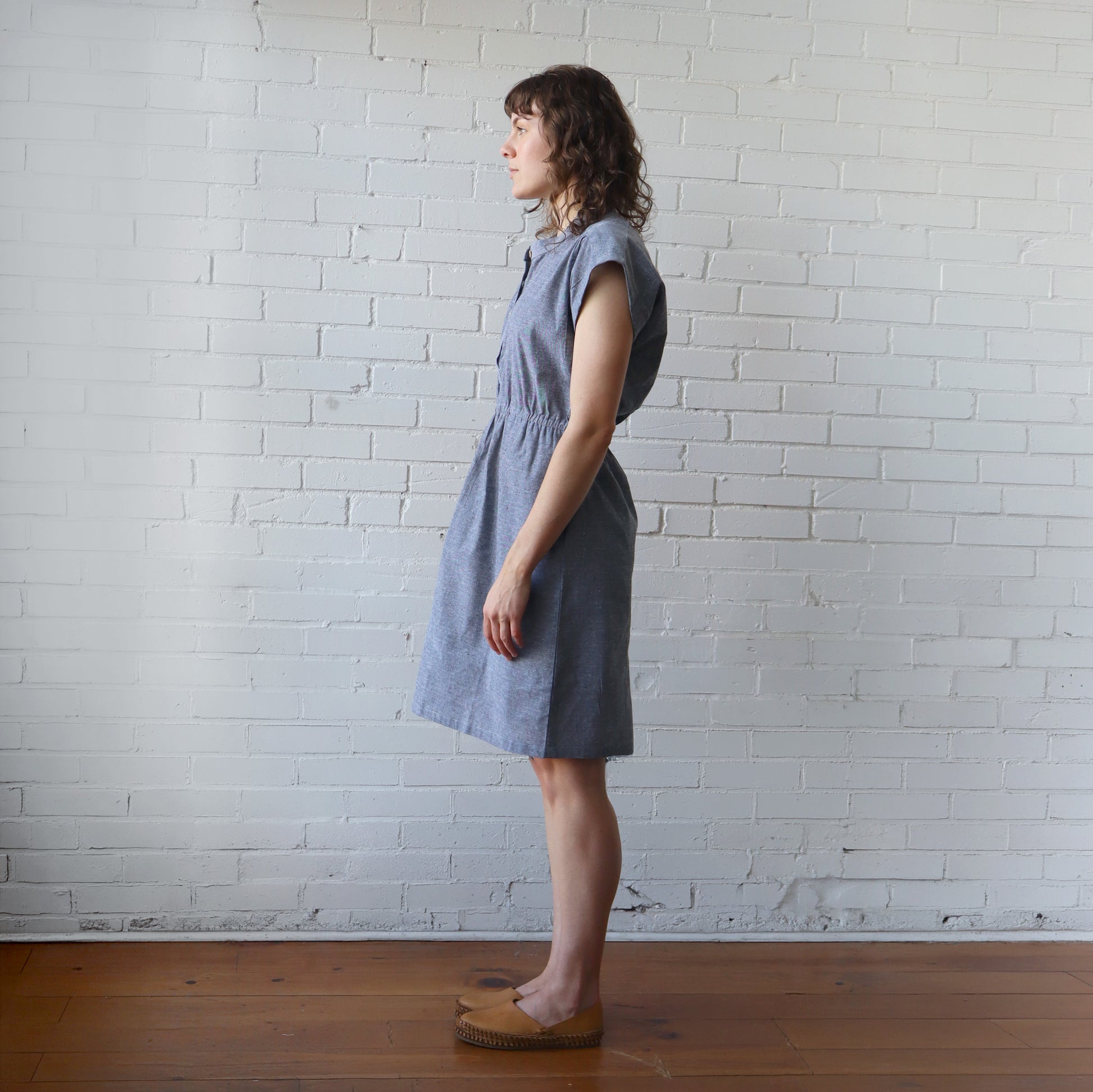 Woman wearing a blue dress standing against a white brick wall.