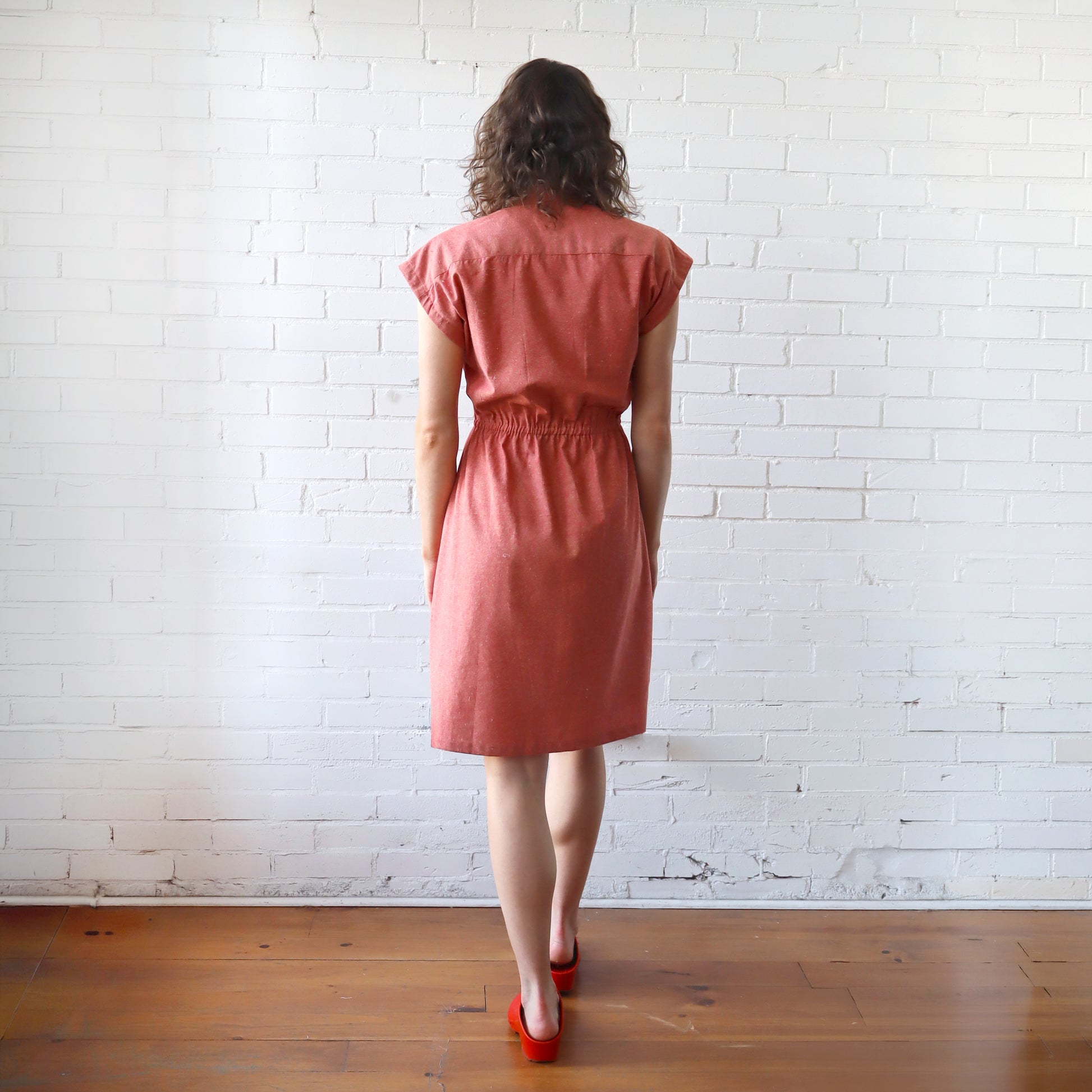 Woman wearing a pink dress standing against a white brick wall.
