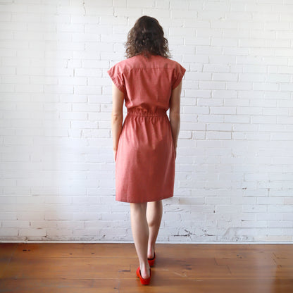 Woman wearing a pink dress standing against a white brick wall.