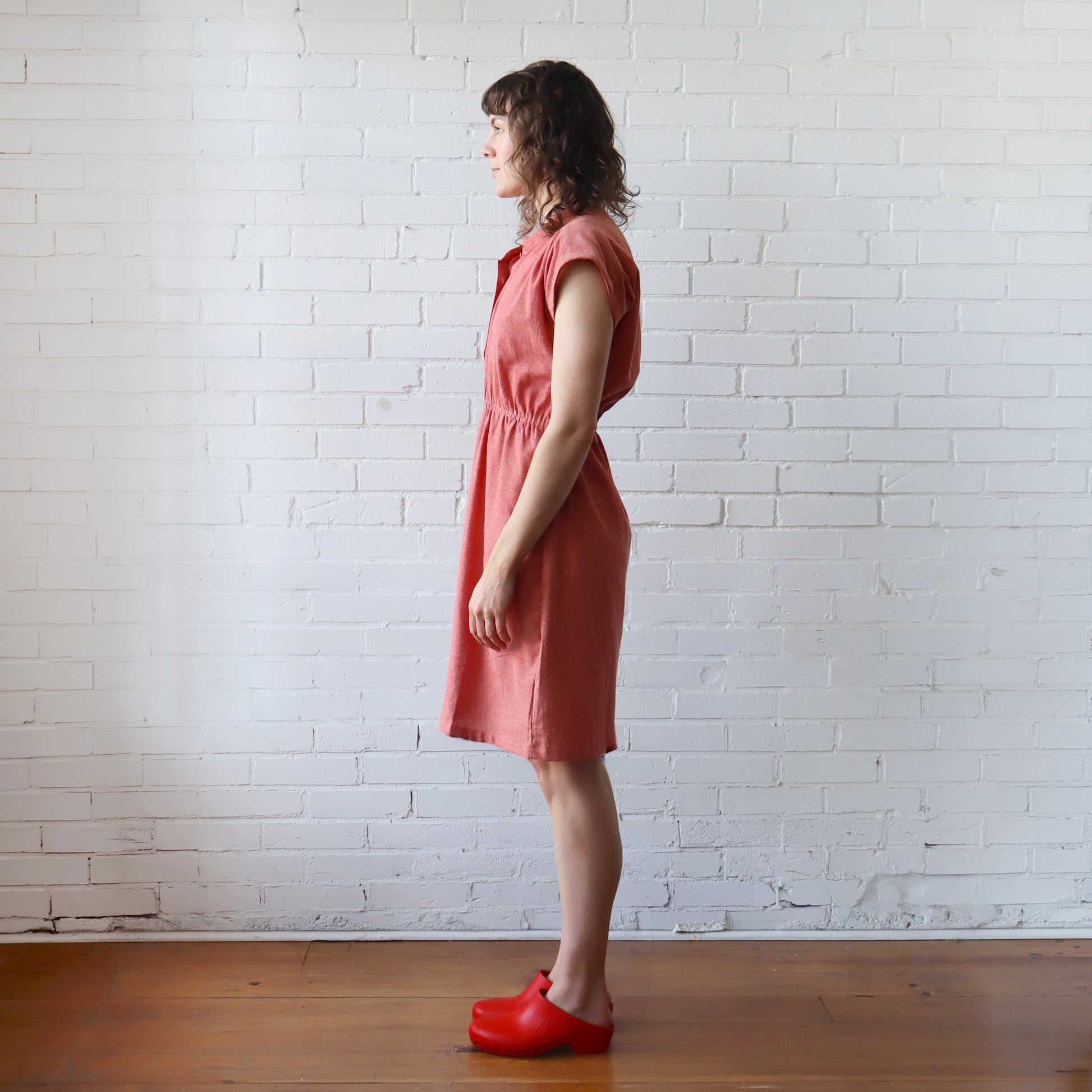 Woman in a pink dress standing against a white brick wall.