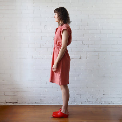 Woman in a pink dress standing against a white brick wall.