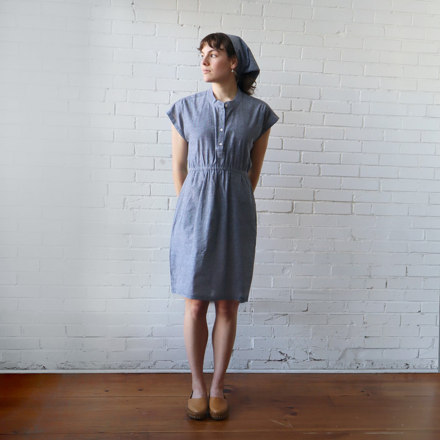 Woman wearing a blue dress standing against a white brick wall.