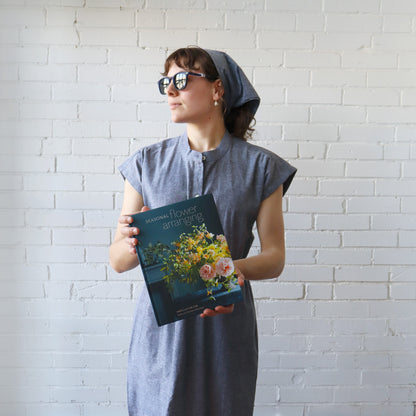 Woman holding a book with floral design against a white brick wall