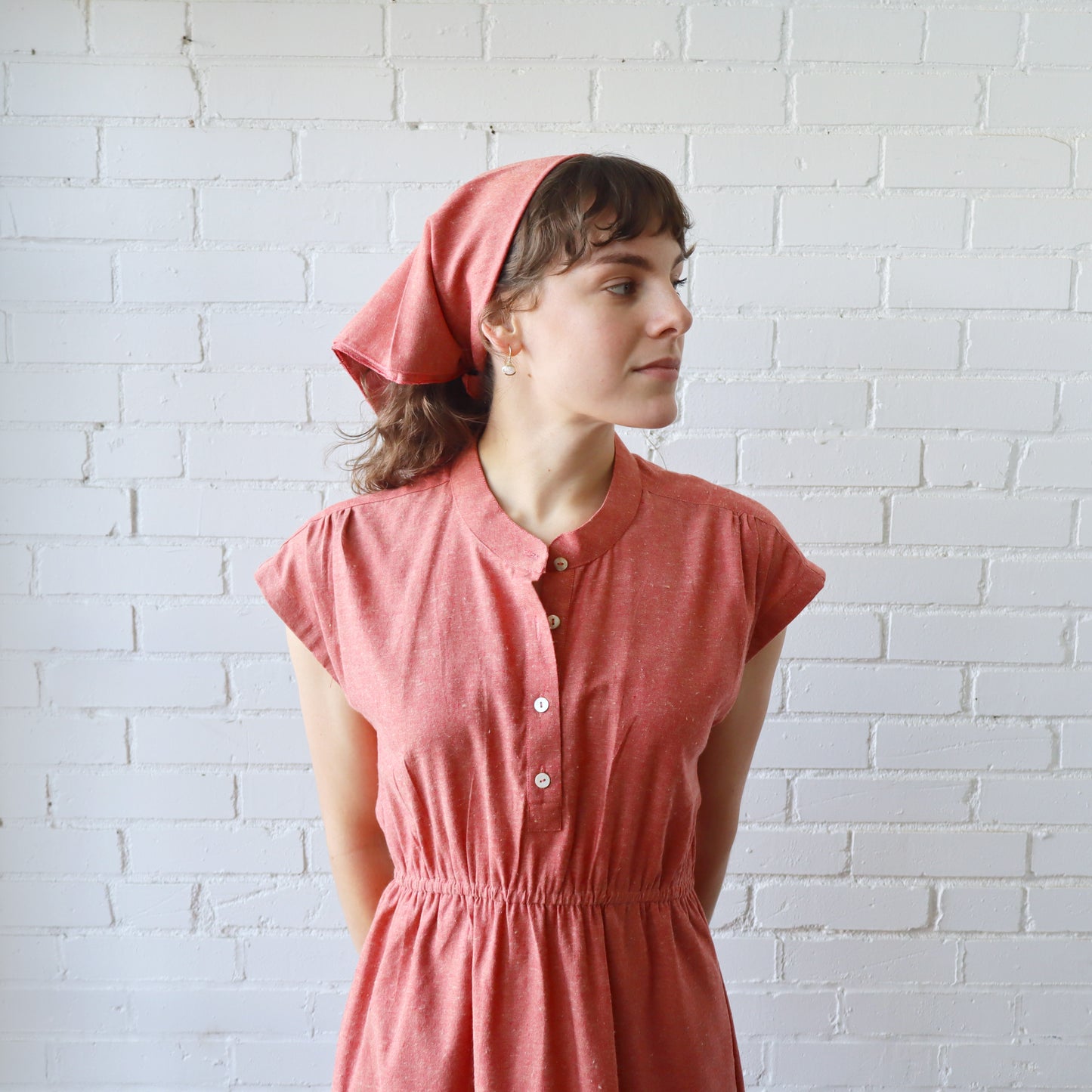 Woman wearing a pink dress and headscarf against a white brick wall