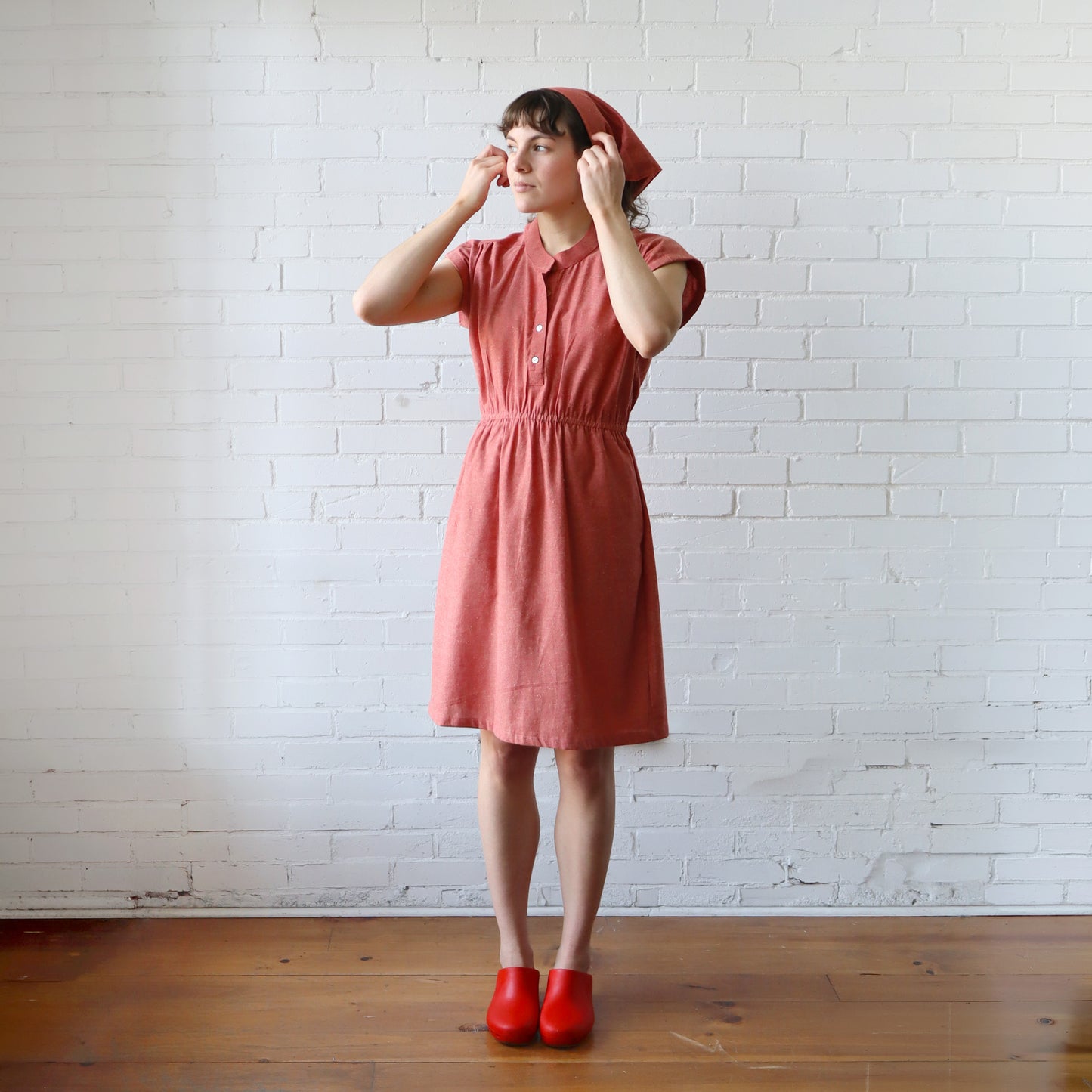 Woman wearing a red dress and red shoes against a white brick wall.