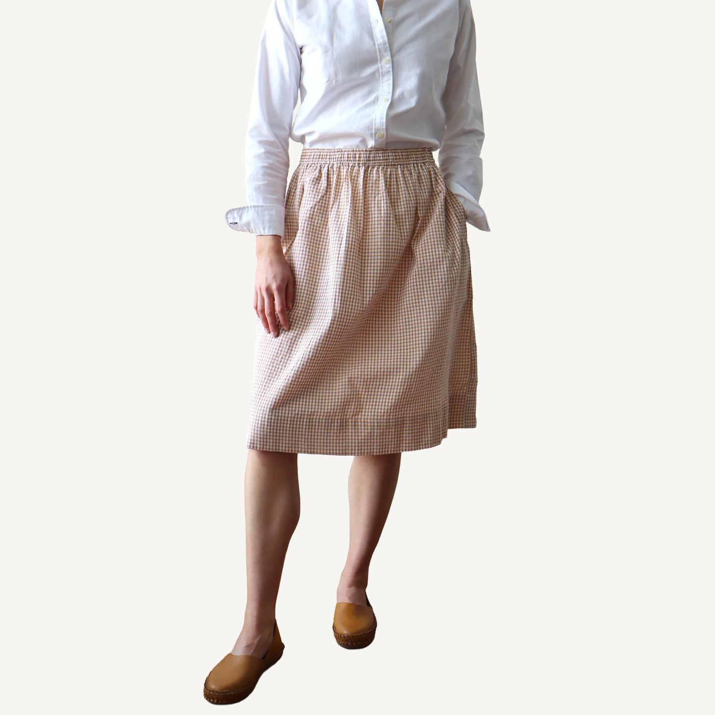 Person wearing a white shirt and beige checkered skirt on a plain background