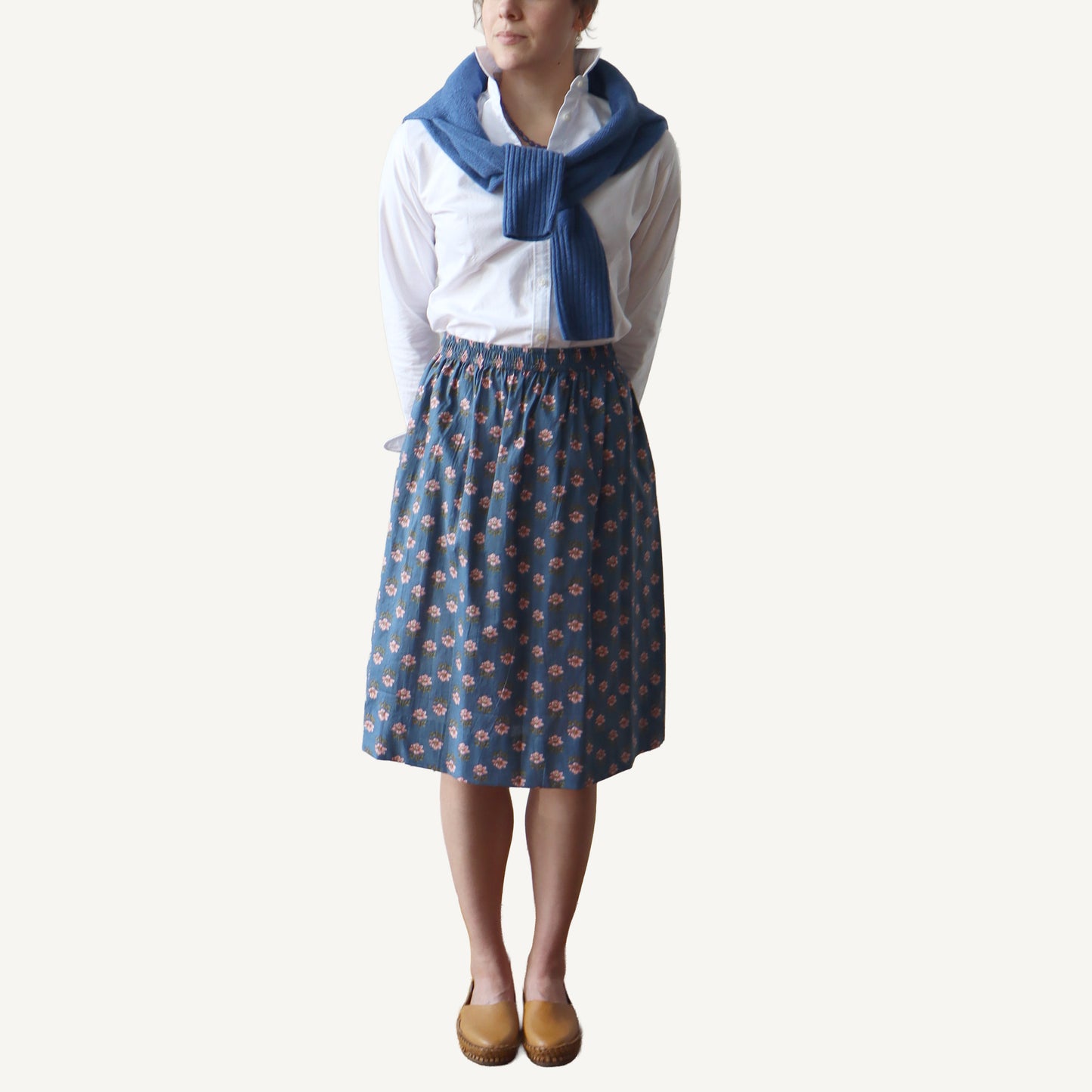 Person wearing a white shirt, blue patterned skirt, and blue scarf on a white background