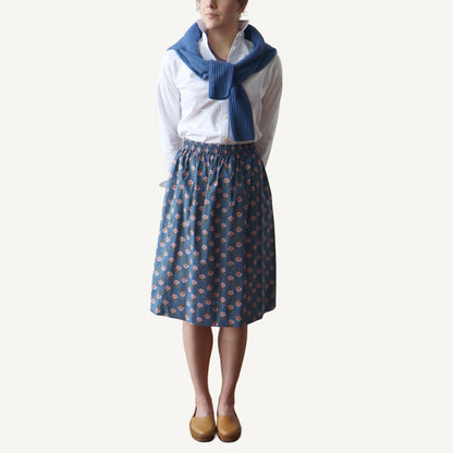 Person wearing a white shirt, blue patterned skirt, and blue scarf on a white background