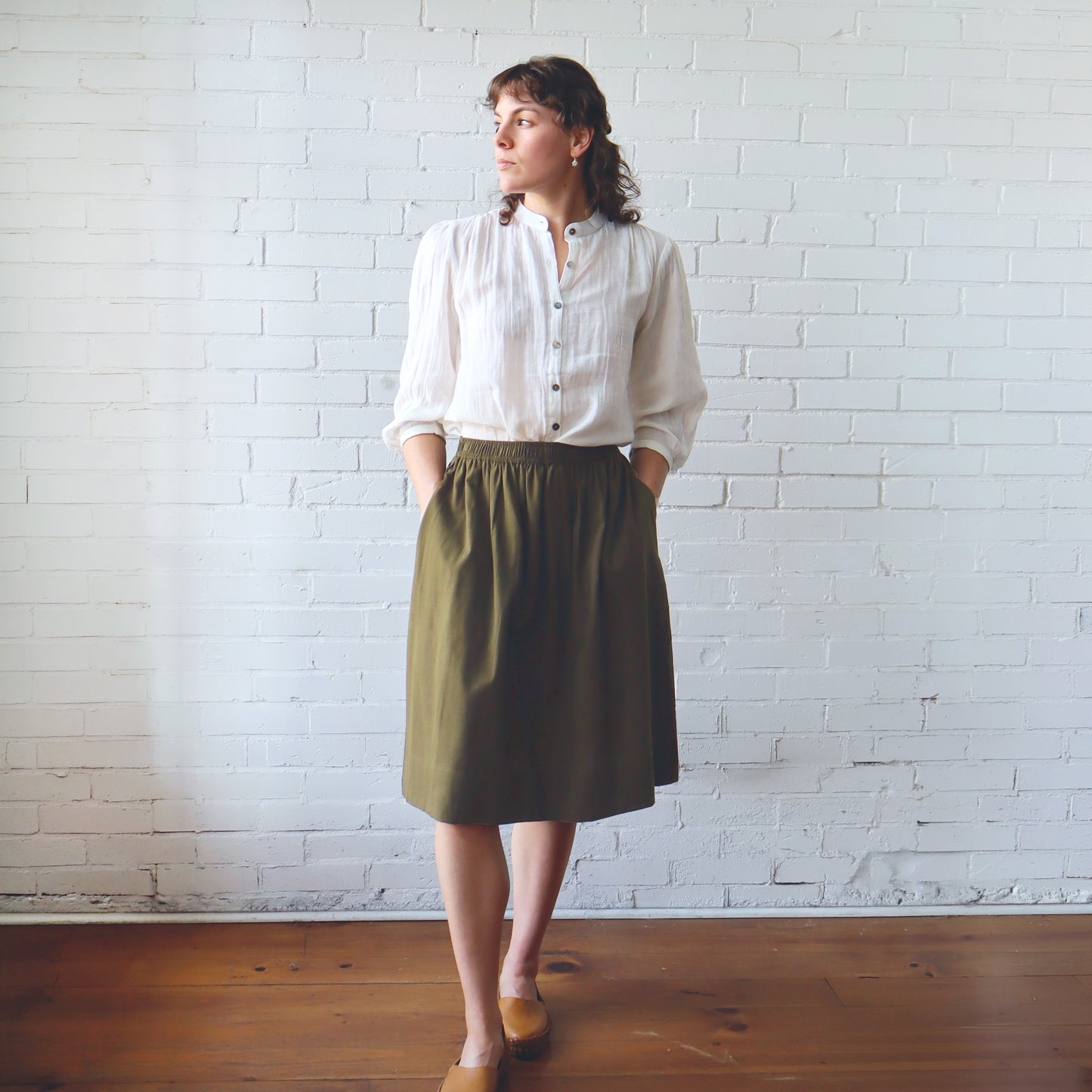 Woman wearing a white shirt and green skirt standing against a white brick wall.