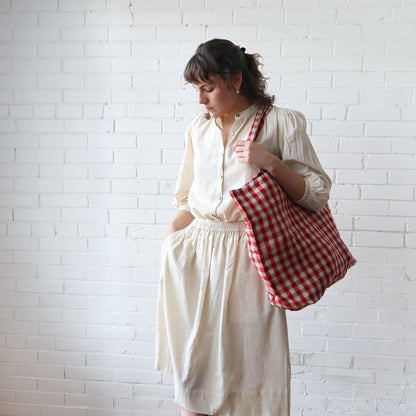 Woman holding a red and white checkered bag against a white brick wall