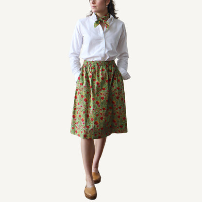 Person wearing a white shirt and green skirt with red pattern on a white background