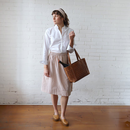 Woman holding a brown tote bag against a white brick wall.