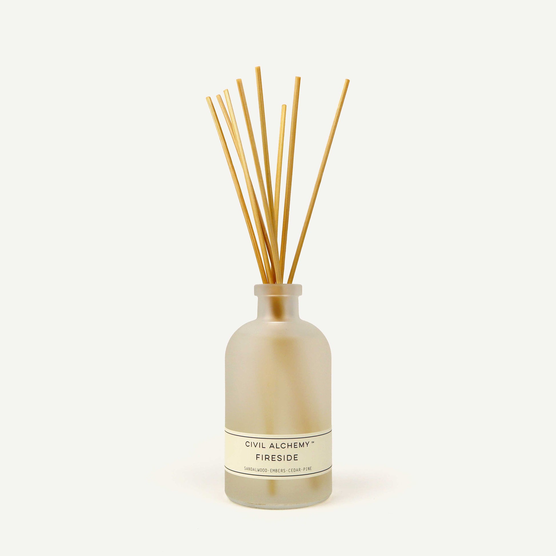 Reed diffuser with wooden sticks in a clear bottle labeled 'Civil Alchemy Fireside' on a white background