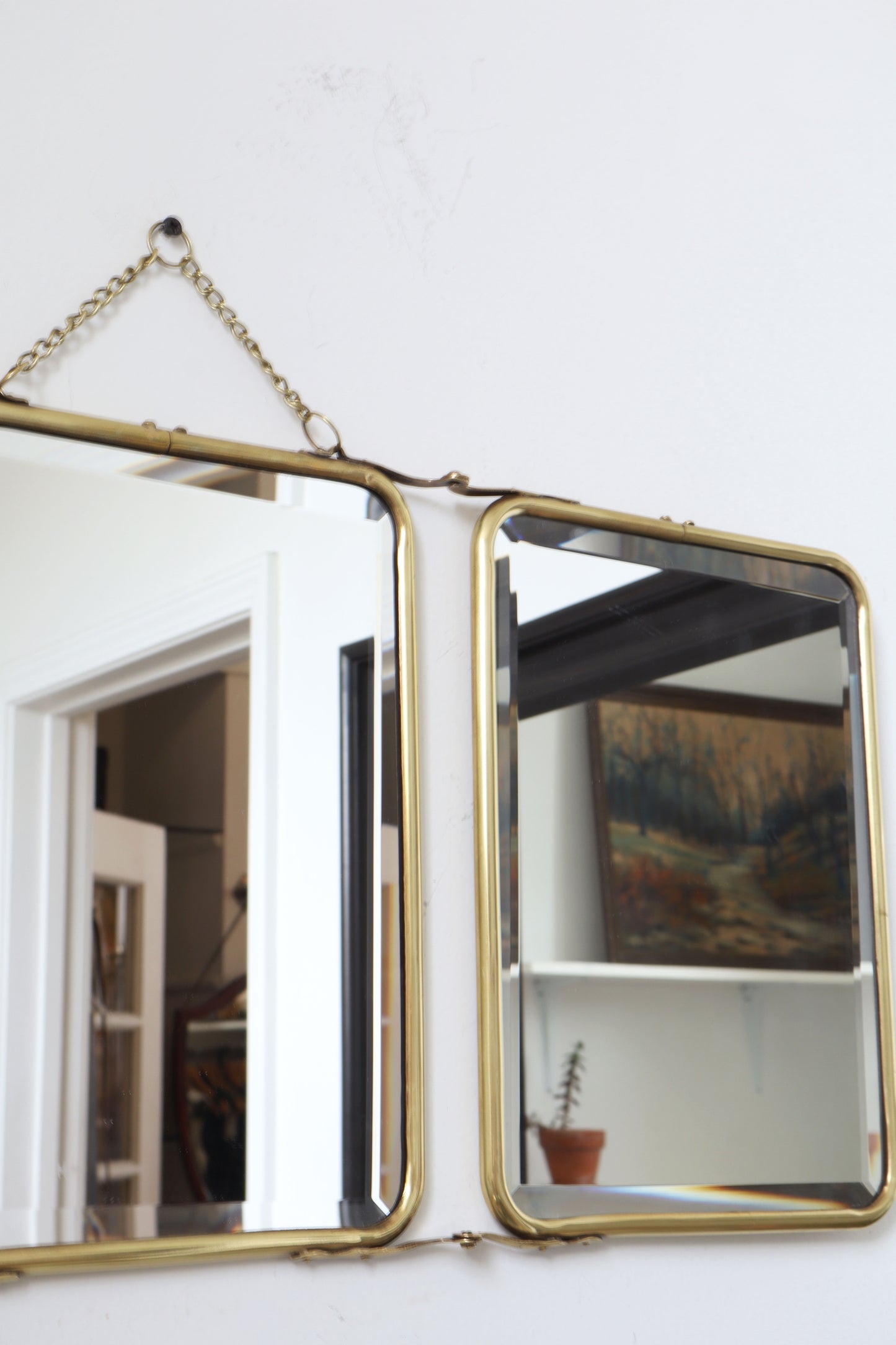 Brass-framed mirror with chain on a white wall