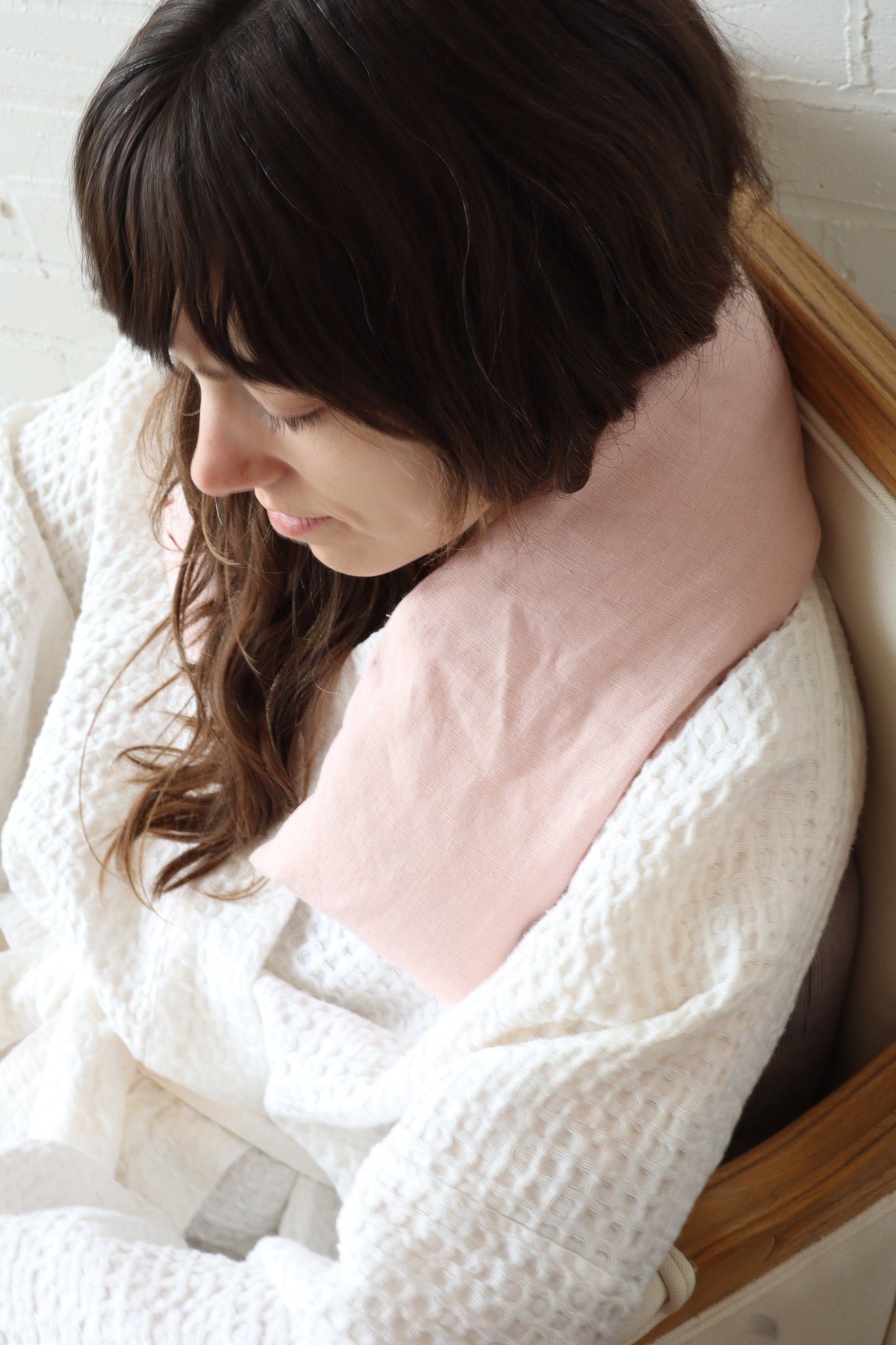 Woman sitting with a pink pillow, wrapped in a white blanket