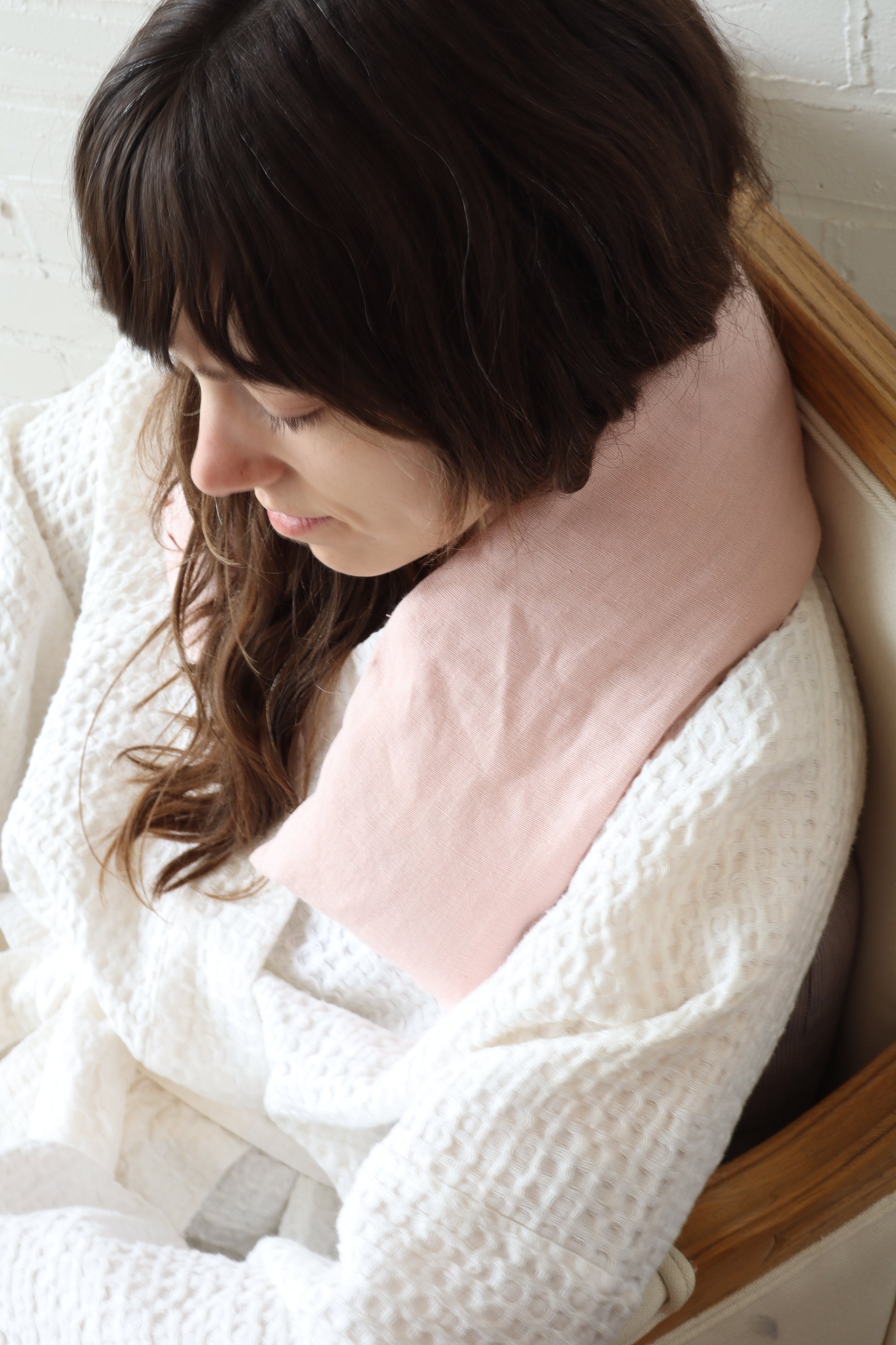 Woman sitting with a pink pillow, wrapped in a white blanket