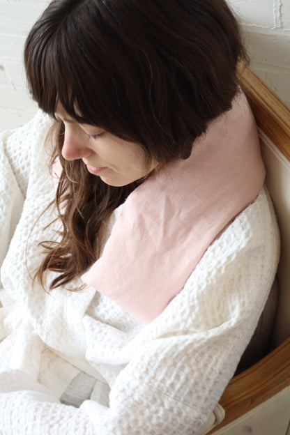 Woman sitting with a pink pillow, wrapped in a white blanket