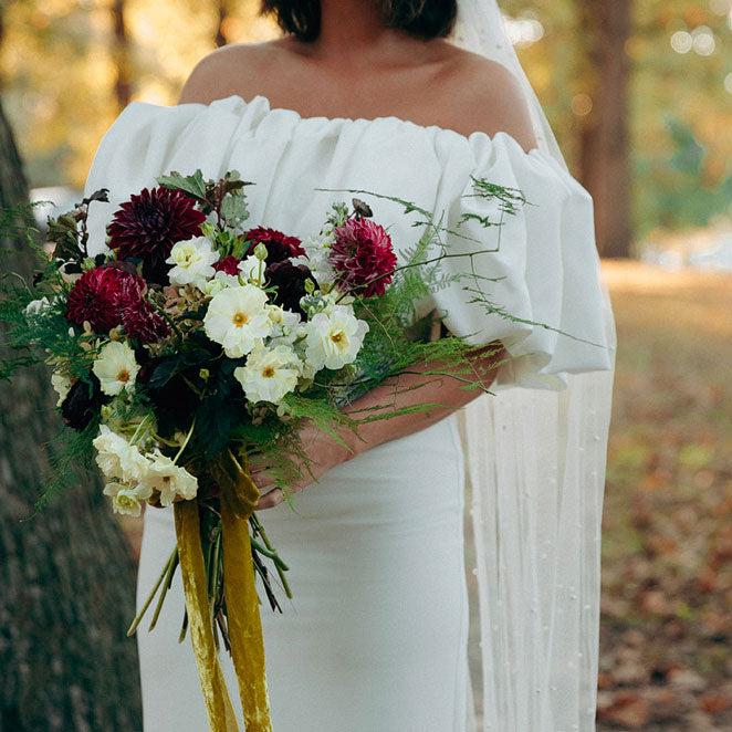 A person in a white dress holding a bouquet of flowers with a variety of colors including red, white, and green.