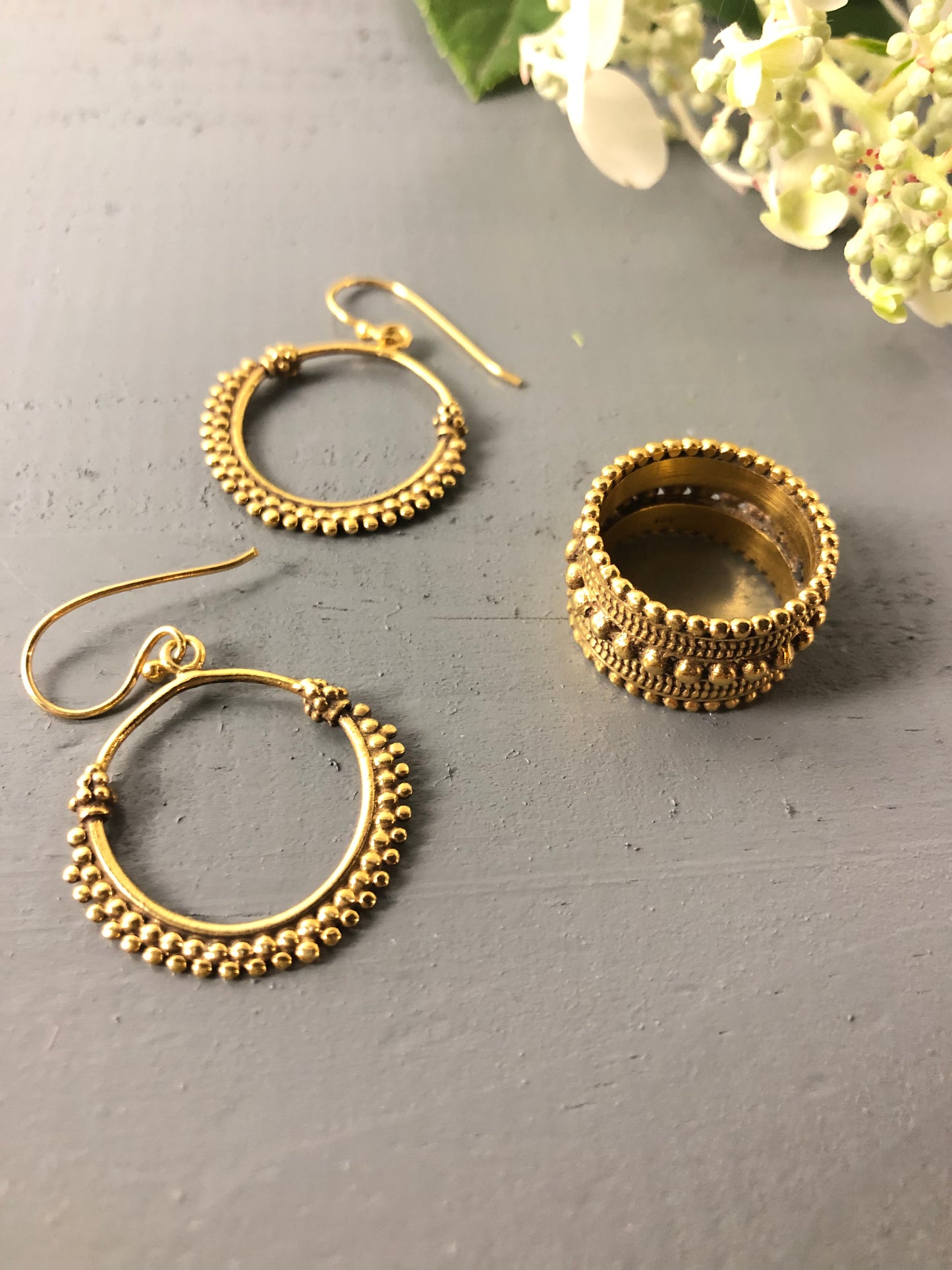 Gold hoop earrings on a gray surface with a blurred floral background