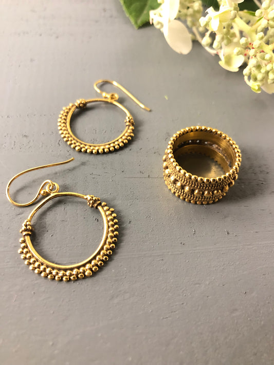 Gold hoop earrings on a gray surface with a blurred floral background