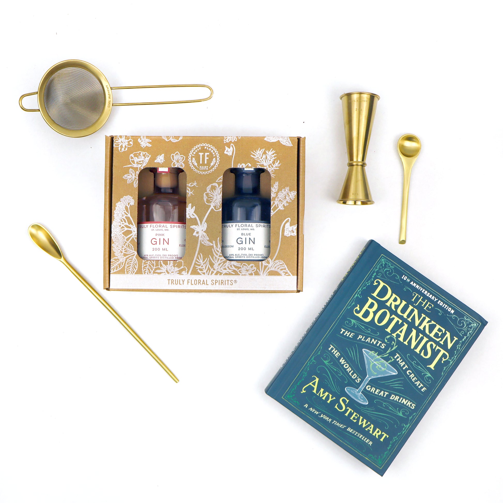 Cocktail kit with gin bottles, jigger, strainer, and 'The Drunken Botanist' book on a white background